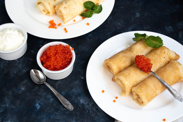 Pancakes stuffed with salted cottage cheese. In the bowl and spoon are red caviar and sour cream. Decorated with mint leaves. 