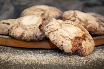 Cookies with powdered sugar on a wooden plate on a dark background close up