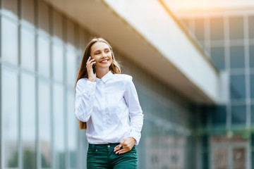 Obraz premium Young famale calling on a smartphone and walking on street. Attractive businesswoman talking by phone. Office building and in the Business District Background. Technology internet and happy people