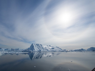 Fototapeta na wymiar Ilulissat Icefjord in Greenland. Dramatic sun halo over glacier reflected in sea water at the Sermeq Kujalleq sea mouth