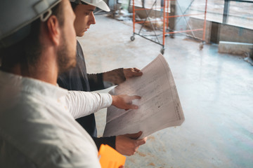 Industrial architect discussing build drawing with worker wearing safety hard hat. Two building engineers lookin at blueprint on construction site