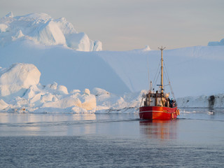 A red fishing boat motors on calm sea with large white glacial ice background - Image