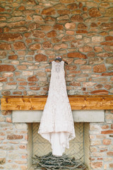 white wedding dress hanging above fireplace, stone wall