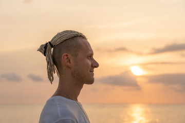 Silhouette of a young guy with dreadlocks on his head near sea during sunset. Close up portrait