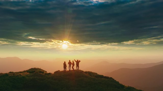 The four people dancing on the mountain with a beautiful sunset