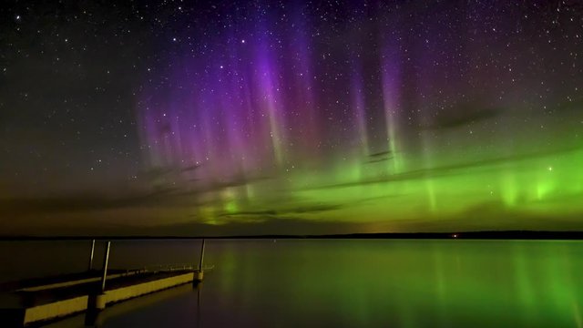 Time lapse of vivid Aurora (Northern Lights) over a calm reflecting lake with a dock in the foreground