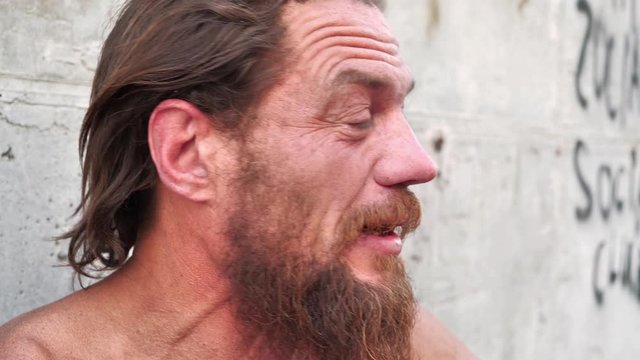 Down-and-out person talks on the camera. Homeless man looks at the camera and talks. Real person with no fixed abode close up