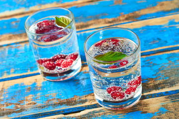 Two transparent glasses full of drinks with leaf and berries lies on weathered blue wooden table