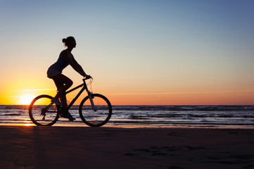 Fototapeta na wymiar Silhouette of sporty woman riding bicycle on multicolored sunset background