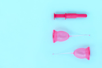 Two pink menstrual cups and an applicator for their introduction on a blue background. Women's Health and Zero Waste Concept