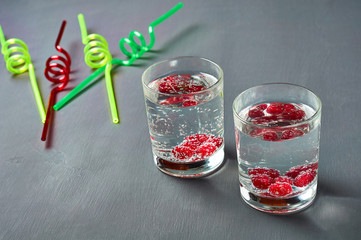 Two transparent glasses full of drinks with red berries near spiral straws lies on scratched dark cement. Space for text