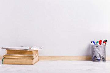 Books, markers, notebook, pencil and glasses on the table against the background of a white board. Copy space.