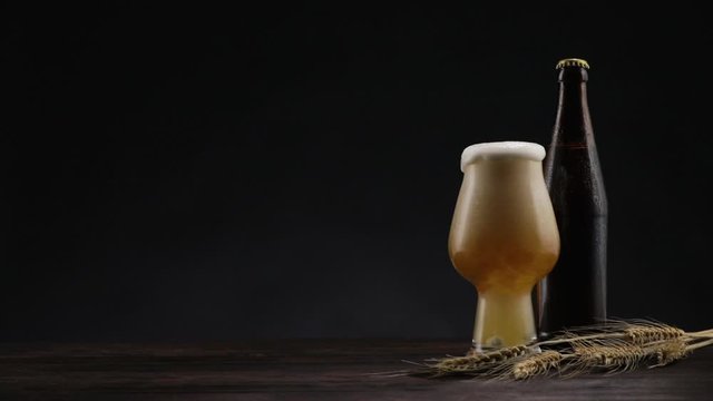 Foaming big stout beer. Stream of beer pours. glass with foaming beer and a bottle with spikelets of wheat on the table. copy space