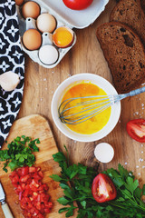 cooking process, ingredients, hearty and healthy breakfast, scramble eggs with tomatoes and herbs on toast with black tea on a wooden background