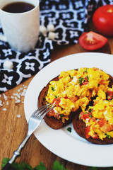 hearty and healthy breakfast, scramble eggs with tomatoes and herbs on toast with black tea on a wooden background