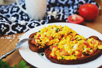 hearty and healthy breakfast, scramble eggs with tomatoes and herbs on toast with black tea on a wooden background