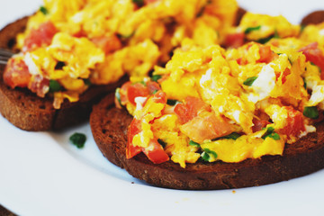 hearty and healthy breakfast, scramble eggs with tomatoes and herbs on toast with black tea on a wooden background