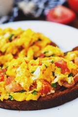 hearty and healthy breakfast, scramble eggs with tomatoes and herbs on toast with black tea on a wooden background