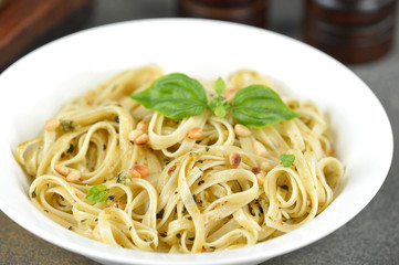 Pasta with pesto sauce. The pasta is decorated with basil greens and pine nuts. A plate with linguine paste occupies the entire space of the frame. Close-up. Macro shot.