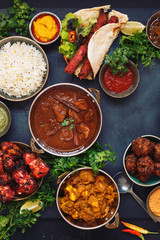 Various Indian dishes featuring  rogan josh, chicken tikka masala,tandoori chicken wings  and  kebabs, with rice and naan bread, top view