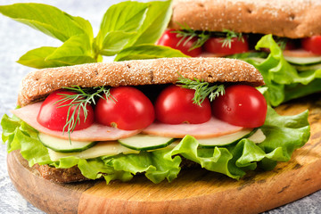 Sandwich with cheese, cucumber and Cherry Tomato on a wooden board. The sandwich is decorated with a lettuce leaf and cherry tomatoes.