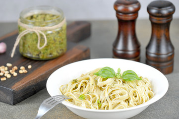 Pasta with pesto and basil. Nearby a jar of pesto, garlic, nuts and seasonings. Lunch table setting concept. Dark background. Close-up.
