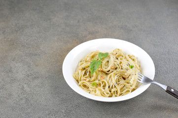 Pasta with pesto sauce. The pasta is decorated with basil greens and pine nuts. A fork is located on the edge of the plate. Free space for text. Close-up.