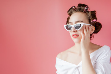 Beautiful girl in hair curlers on pink background