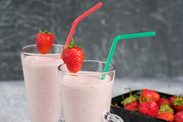 Two glasses with strawberry milkshake with pieces of berries on the edge of the glass on gray background.