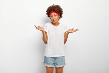 Uncertain clueless female with Afro hairstyle, spreads hands with doubt, cannot make decision,...
