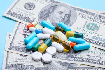 Pile of colorful capsules pills on dollar bills on blue medical table. Concept of expensive medicine, treatment, medical insurance