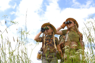 Two young girls seem to be on safari.They observe  the outdoor countryside area. They are dressed...