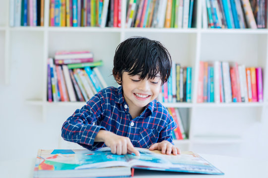Happy little boy reading a book in the library