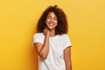 Happy lifestyle concept. Pleasant looking funny Afro woman feels lucky and satisfied, laughs happily, has white teeth with small gap, enjoys awesome day off, stands against yellow background