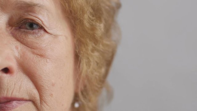 half face of an elderly serious woman looking straight, grandmother blinking eye tiredly, concept people age and health