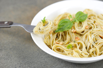 Pasta with pesto sauce. The pasta is decorated with basil greens and pine nuts. A fork is located on the edge of the plate. Free space for text. Close-up....