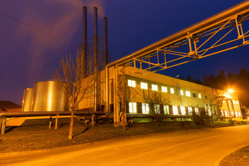  Building of a modern industrial boiler room factory at night. Yellow lighting from lanterns and blue sky. Pipes, pipelines, smoke from the chimney