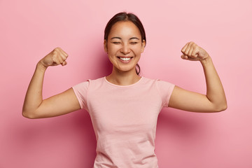 Strong powerful Asian woman with dark combed hair, toothy smile, raises arms and shows biceps, has...