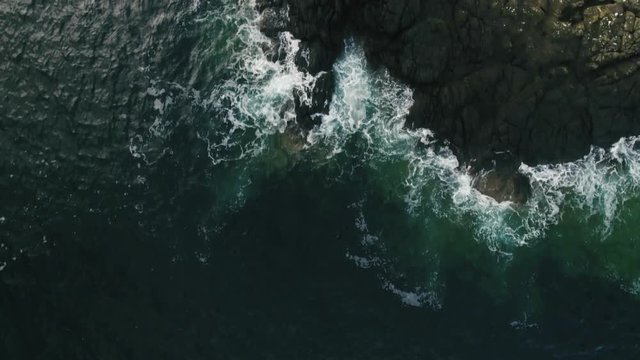 Aerial view on waves smashing on the rocks, clear water, camera looking down