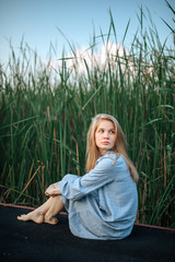Romantic girl in blue dress seating on pier. Vegetative background