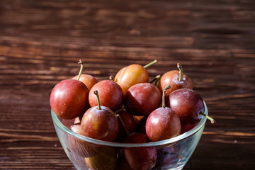 Ripe sweet plum fruits in glass bowl on dark moody wood table background, hard light, copy space