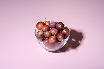 Ripe sweet plum fruits in glass bowl on pink background, hard light, copy space