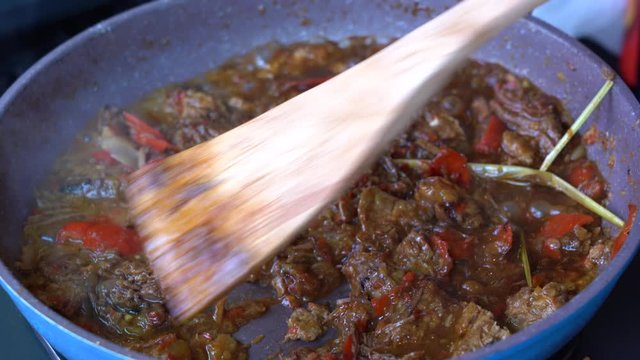 Frying pan with onion, lemongrass, red pepper and beef meat, close up. Indonesia. Sambal Goreng Ati Kentang, Indonesian cuisine, spicy beef meet and potatoes garnish with lemongrass leaf and red chili