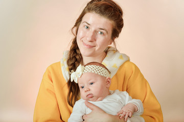 Mom holds the baby in her arms and poses for the camera in the studio, the concept of love and unity and care for loved ones and younger ones.