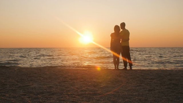 silhouette of a romantic young couple standing hugging on the seashore, man and woman enjoying sunrise on the beach, summer vacation and love