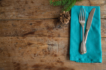 Festive place setting for christmas dinner. Vintage cutlery on the blue napkin and fir twig with cone on the old wooden background with copy space