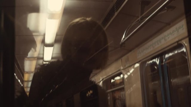 A young blonde with glasses rides in a subway car. Video shooting from a neighboring carriage.