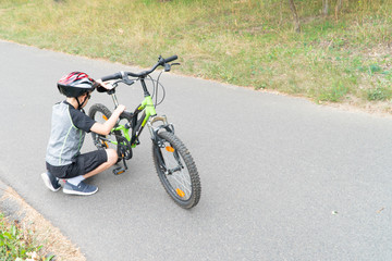 Obraz premium School boy in the protective helmet fix bike on the road.