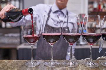 The bartender pours red wine
