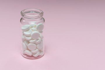 White tablets in glass bottle on pink background. Health care and treatment concept. Copy space for your text. Template for medical blog, social media.